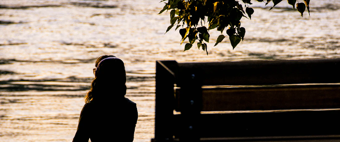 silhouette of person sitting on bench near body of water during daytime